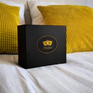 Coffret élégant noir avec au milieu une étiquette en cercle, avec l'image du masque loup en dentelle de couleur or