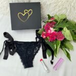Image de la Love Box Séduction avec le logo Loving Up au centre, accompagnée d'un joli bouquet de roses ainsi que d'une culotte en dentelle noire très sexy avec des nœuds à nouer. À côté, un beau rouge à lèvres vibromasseur.