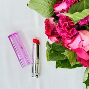 Image du rouge à lèvres vibrant de couleur rose bonbon accompagnée d'un joli bouquet de roses.