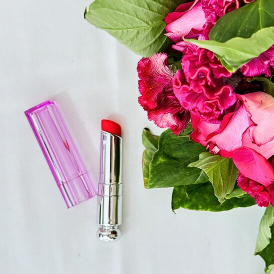 Image du rouge à lèvres vibrant de couleur rose bonbon accompagnée d'un joli bouquet de roses.