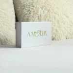 Un coffret blanc élégant, orné au centre du mot "Amour" gravé en or, et intégrant le logo de la marque Loving Up.